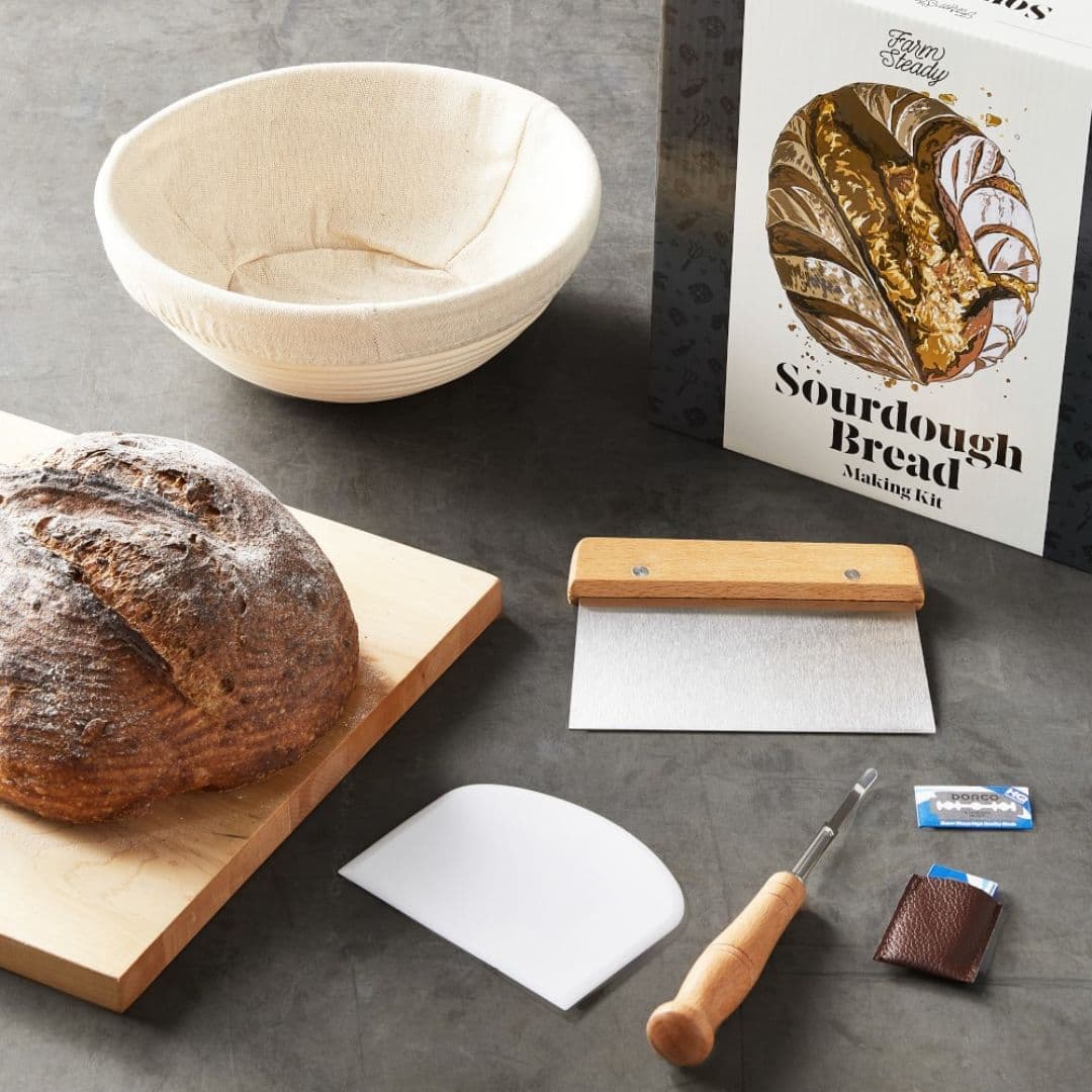 DIY sourdough bread making kit from Williams Sonoma with proofing basket, fresh baked loaf, scraper, and dough tools.